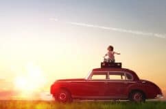 chlid on top of a classic parked car with a suit case