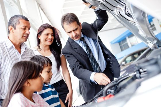 family looking at used car engine to buy it with salesman