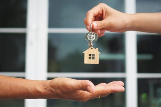 hand giving house keys to another hand with a house shaped keychain