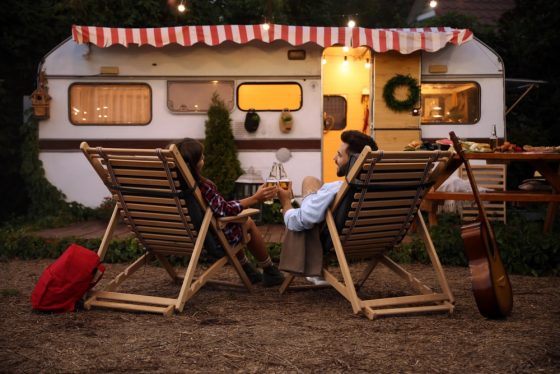 Millennial couple sits by fire outside of camper