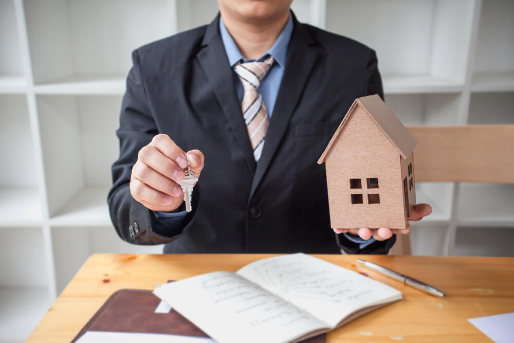 A real estate agent holds house keys and a small model home above signed documents, highlighting the importance of renters insurance when leasing a new place.