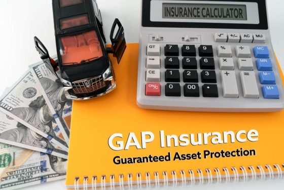 Calculator, cash, and a toy car next to a notebook labeled GAP insurance, representing cost considerations for GAP insurance California coverage.