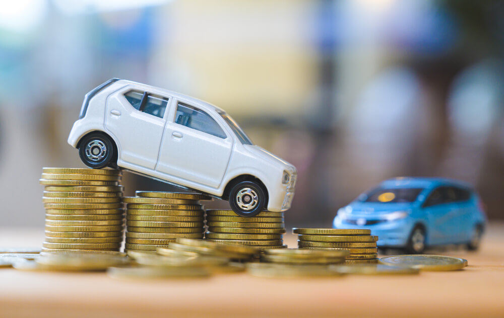 Small toy car positioned on stacks of coins, illustrating how GAP insurance California helps cover the difference between a car’s value and loan balance.