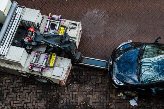 A car being lifted by a tow truck from a residential street, illustrating a situation where a car towed in California may require recovery steps.