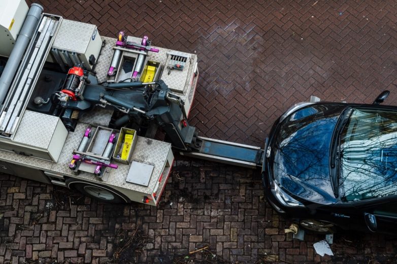 A car being lifted by a tow truck from a residential street, illustrating a situation where a car towed in California may require recovery steps.