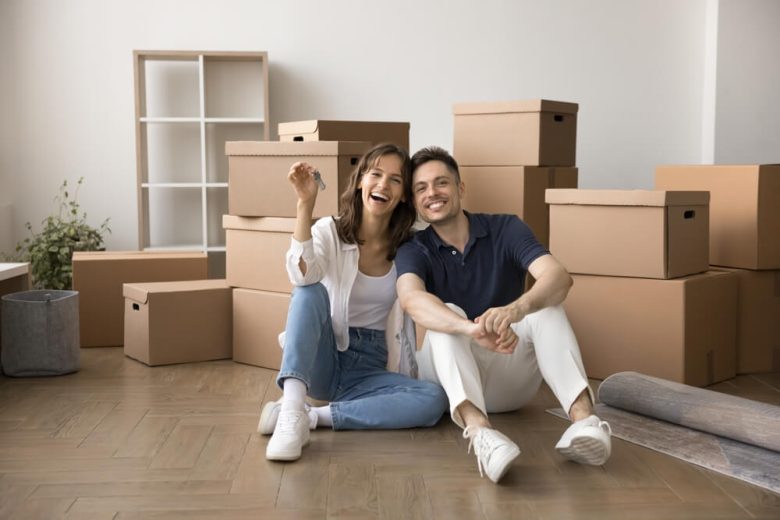 Happy couple sitting among moving boxes in a new home, highlighting the importance of renters insurance for protecting belongings.