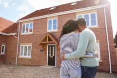 African-American couple stands in front of home they want to buy with their backs to the camera