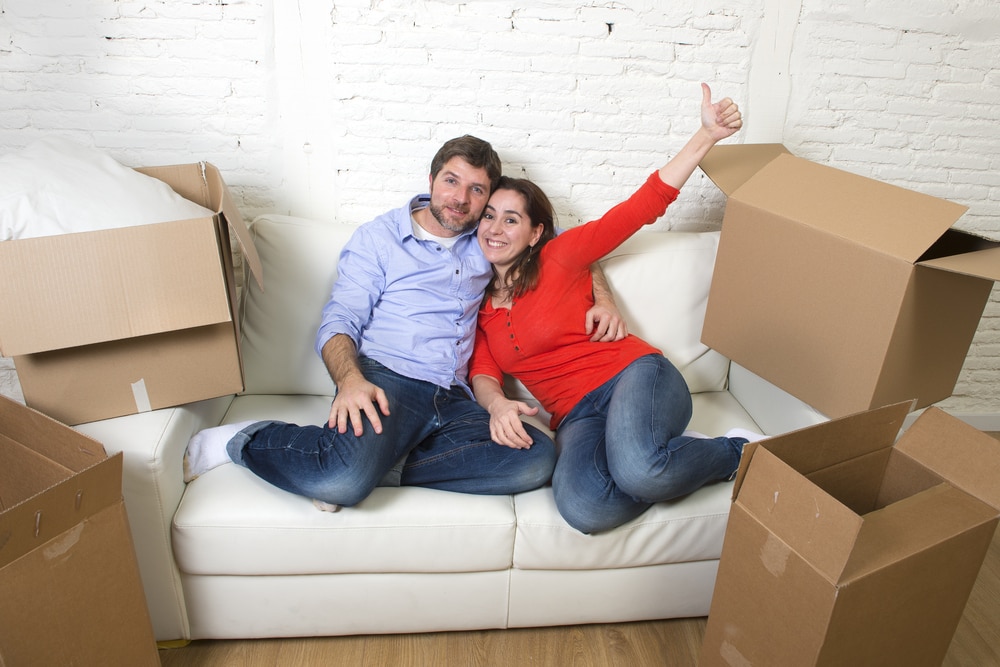 Young happy American couple lying on couch unpacking boxes having fun together celebrating moving in a new apartment