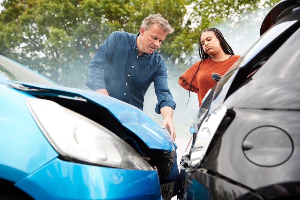 Man looks at damage while aggravated woman looks on after car wreck