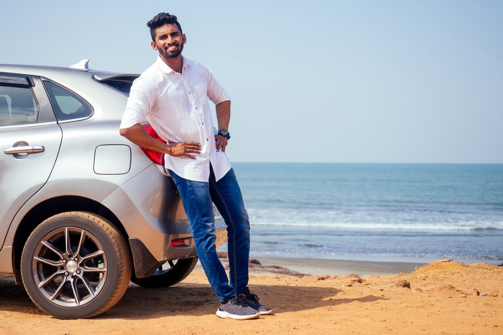 Indian man leans against his new car at the beach