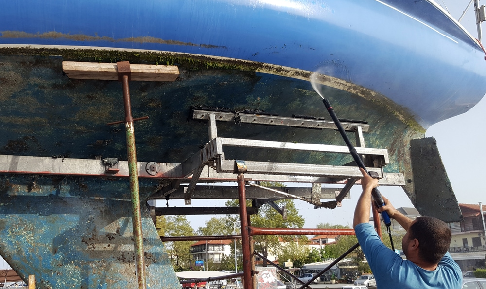 Man washes the bottom of a sailboat with a pressure washer