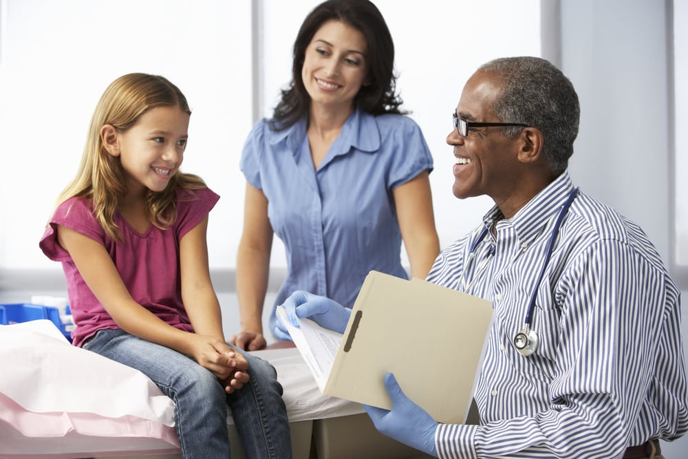 An African-American medical practitioner checks on a young girl while her mother looks on in an exam room