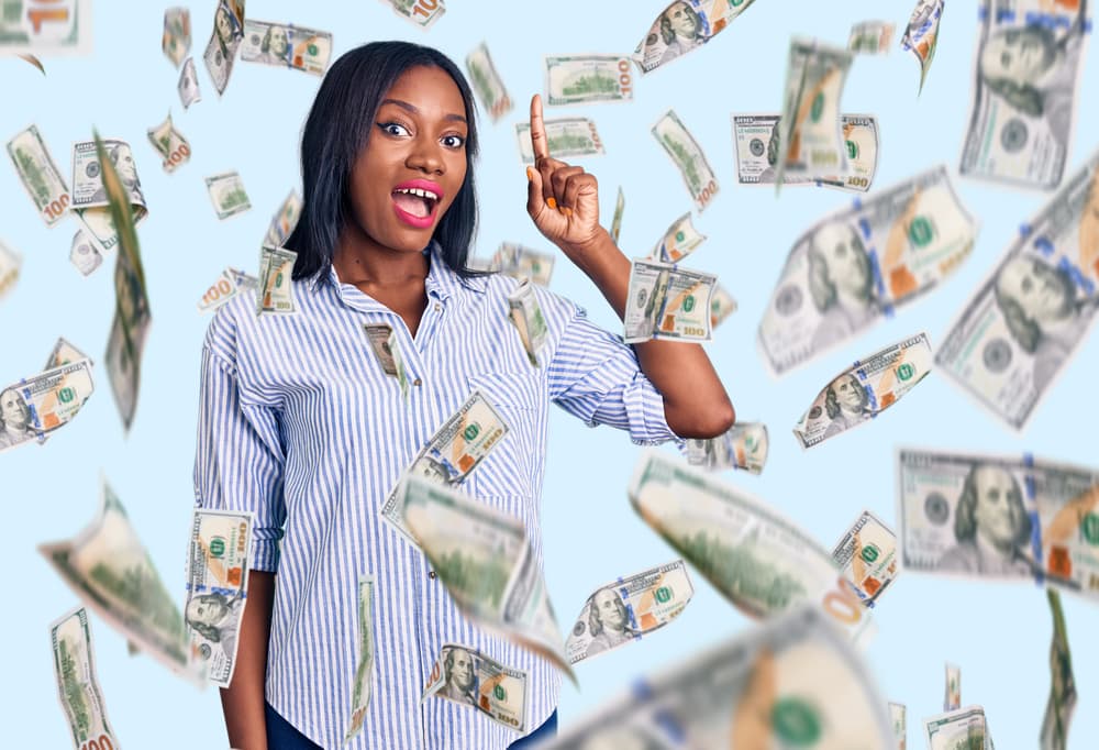 Happy African American woman points up for a good idea while money floats around her