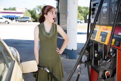 Young woman pumping gas looks stressed at the price