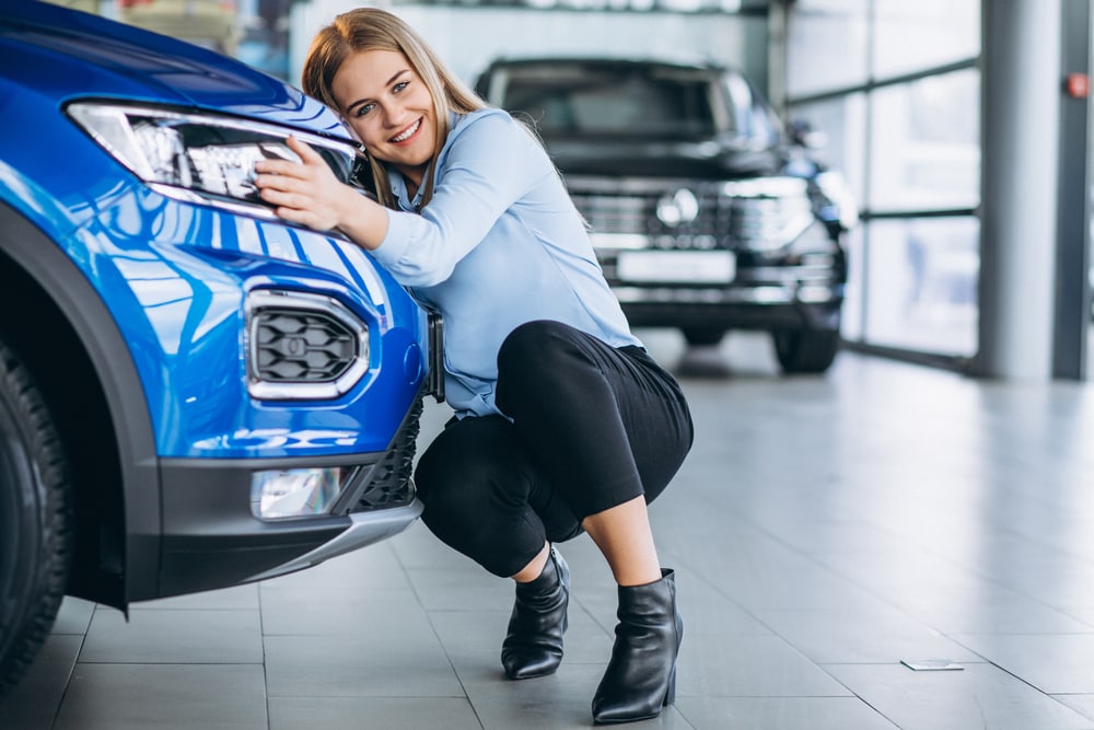 Young woman hugs the front fender of her new car