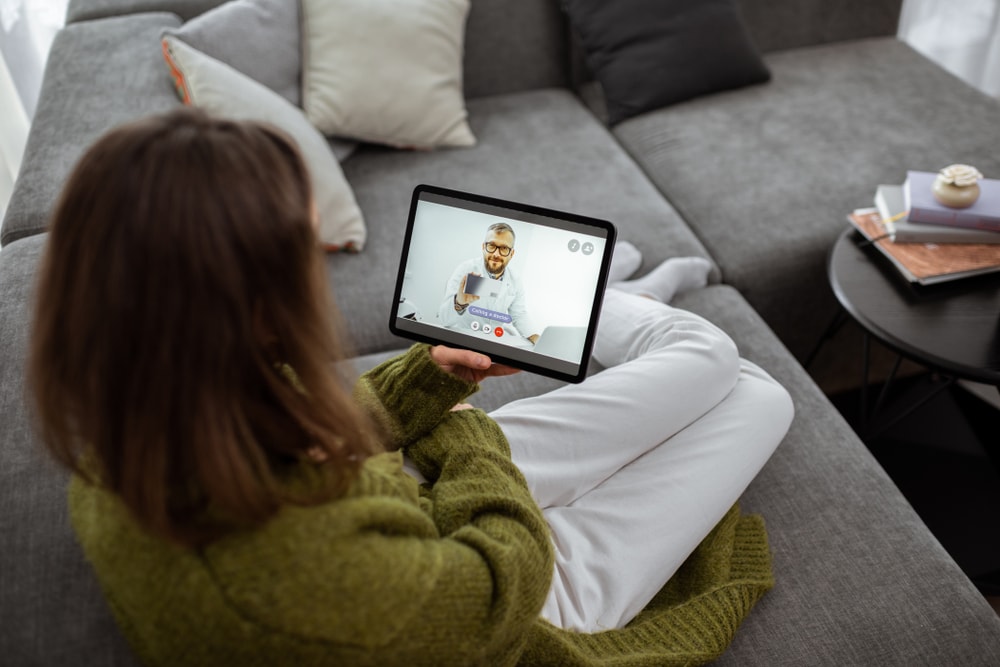 Woman sitting on couch talking to a doctor online - health insurance in California