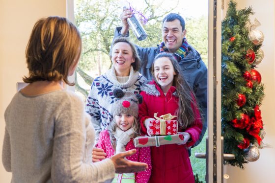 Family comes to visit for the holidays, family of four with gifts at door with surprised woman answering door - home insurance in California