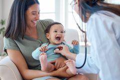 Smiling mom holds happy baby while doctor does an exam