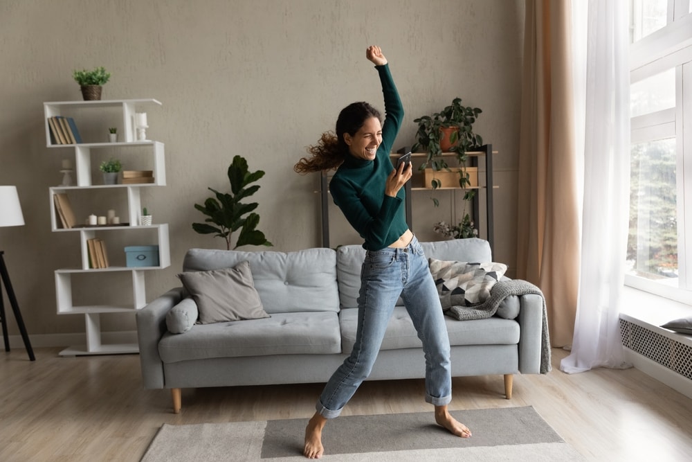 Young woman dancing to music in her apartment living room - cheap renters insurance in California.