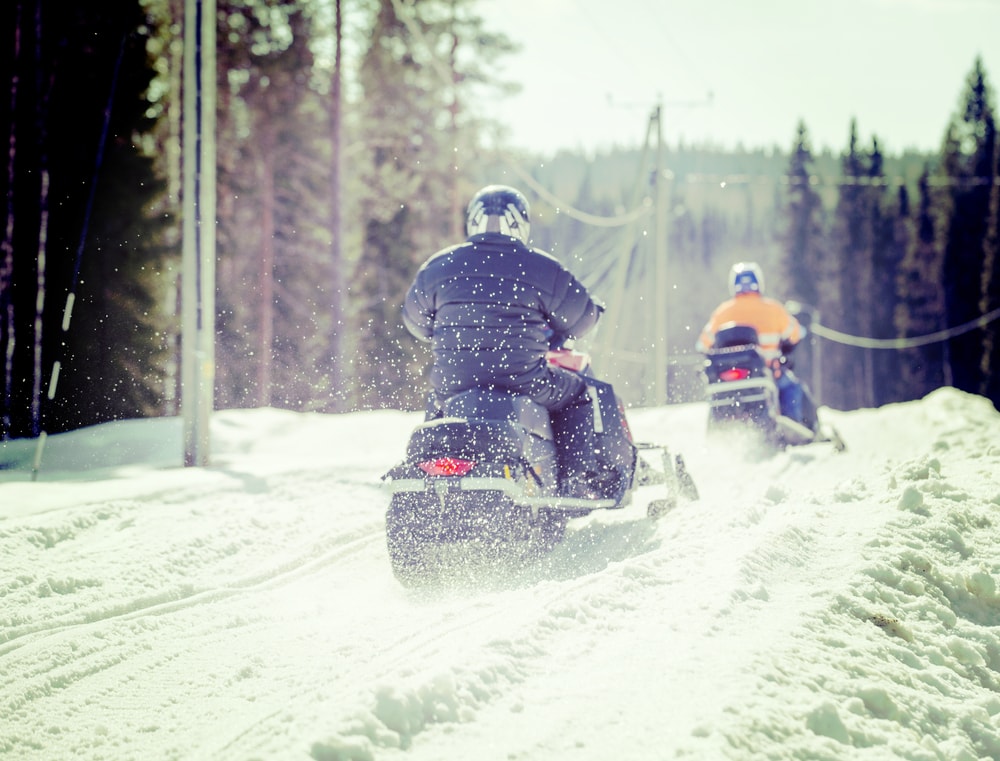 Two snowmobiles from behind driving along a snowy path - cheap snowmobile insurance in California.