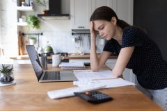 Young woman at her laptop stressing over high car insurance bill, cheap car insurance in California.