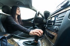 Woman behind the wheel shifting gears with her right hand.