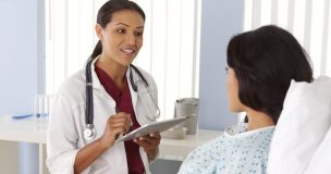 Smiling female doctor talks to woman in hospital bed.