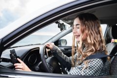 Young female driver using a mounted smartphone while seated in a car, illustrating car insurance considerations for teenagers.