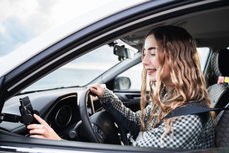 Young female driver using a mounted smartphone while seated in a car, illustrating car insurance considerations for teenagers.