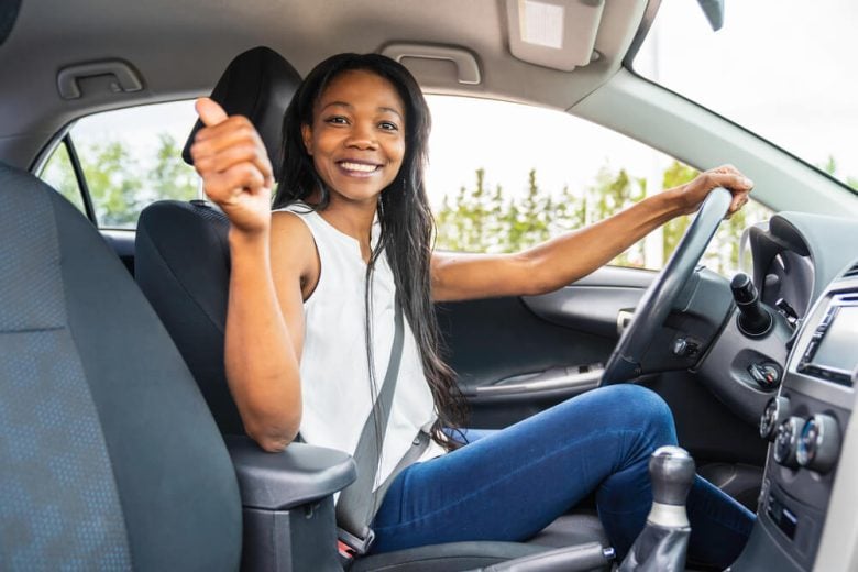 Young smiling African-American girl behind the wheel of the car.