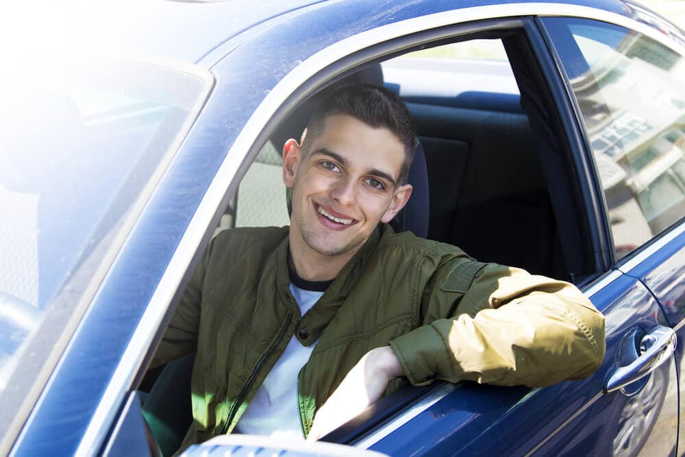 Young man smiling behind the wheel of the car.