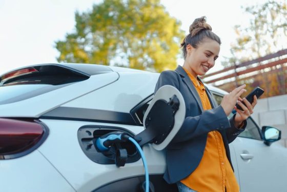 Young women on her phone while charging her electric car.
