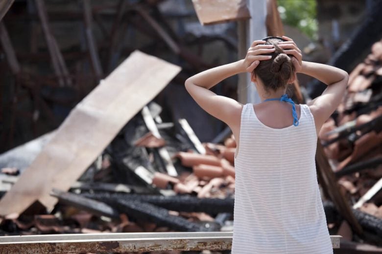 Woman with her hands on her head from behind standing in front of the ruins of her home after a tornado - cheap home insurance in CA.