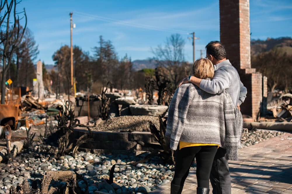 Husband and wife standing together looking at the remains of their home after a fire - cheap home insurance in CA.