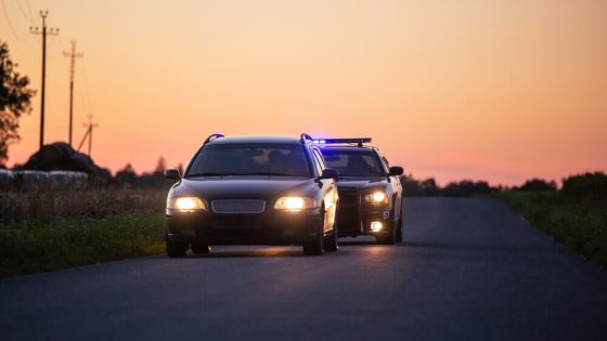 Police car with flashing lights pulls over a sedan on a rural road at sunset, illustrating ticket vs. citation in California.