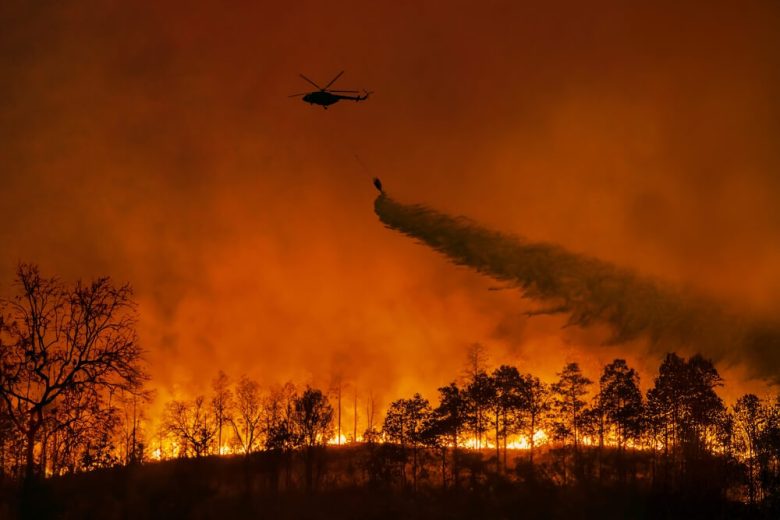 An airplane flies over a wildfire and drops water.