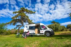 A woman relaxes outside of her RV in a beautiful setting - cheap RV insurance in California.