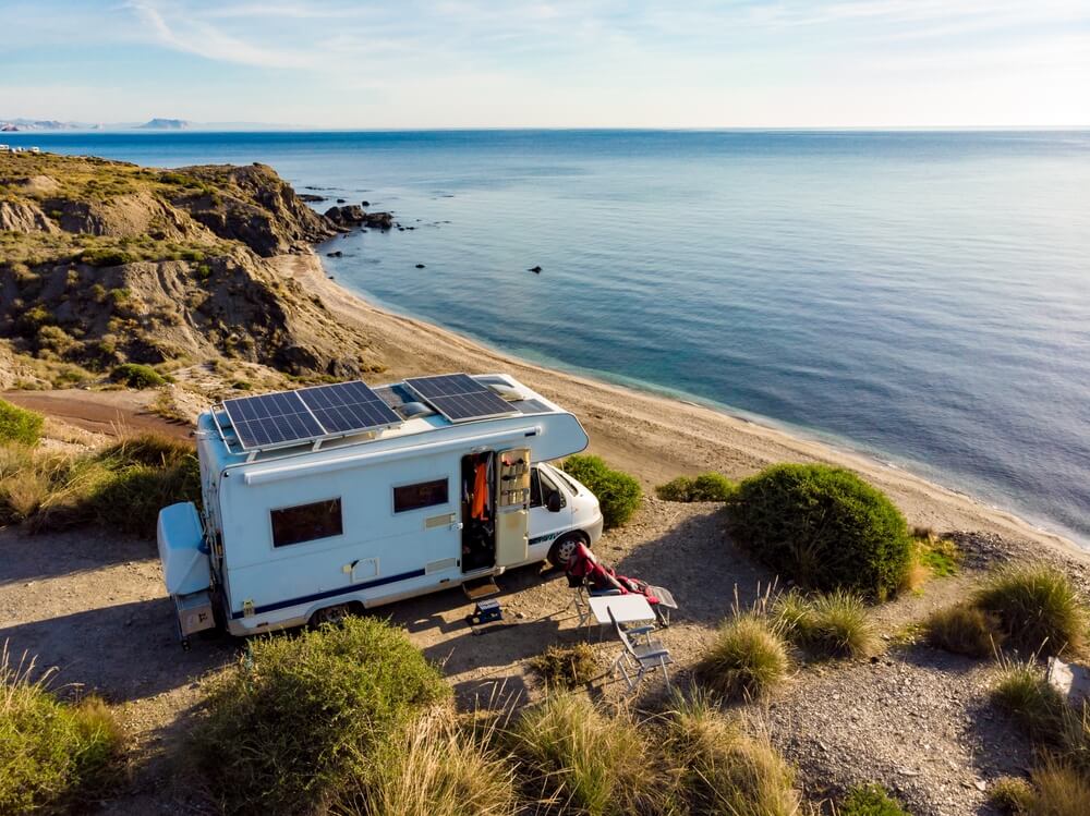 An RV with solar panels is parked by the water in California - cheap RV insurance.