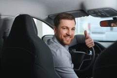 A man turns around to give the thumbs up to someone in the back seat - cheap uninsured motorist coverage in California.