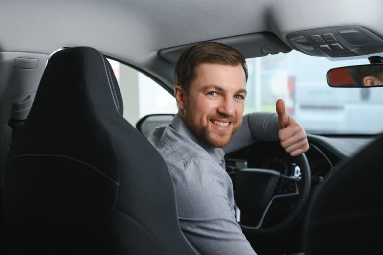 A man turns around to give the thumbs up to someone in the back seat - cheap uninsured motorist coverage in California.
