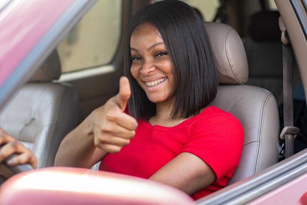 A woman gives a thumbs up behind the wheel of her car - cheap uninsured motorist coverage in California.