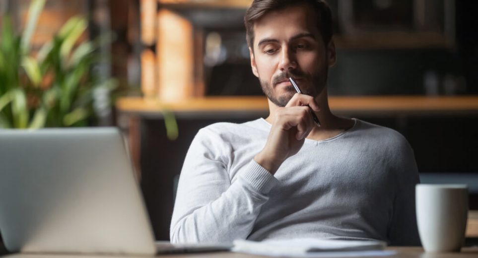 Pensive man sits and looks at his laptop trying to figure out hjow to switch car insurance companies - cheap car insurance in California.