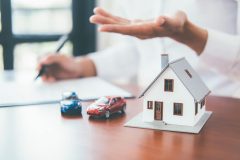 Concept of bundling insurance to save money, hands with small fake house and toy cars together on table - cheap car insurance and discounts in California.