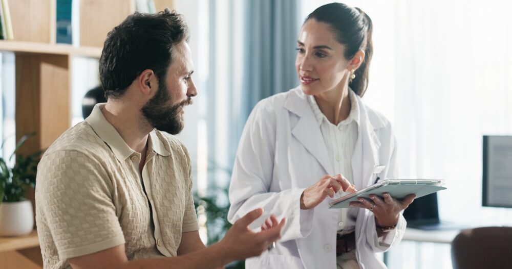 Doctor, patient or consulting with tablet for health advice, checkup or visit at clinic appointment. Man, and medical worker with technology for examination, results or diagnosis at hospital. Free or low-cost health insurance in California.