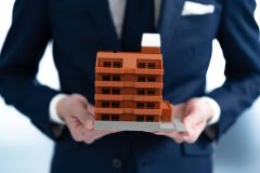 Man's hands holding miniature apartment building, importance of renters insurance in California.