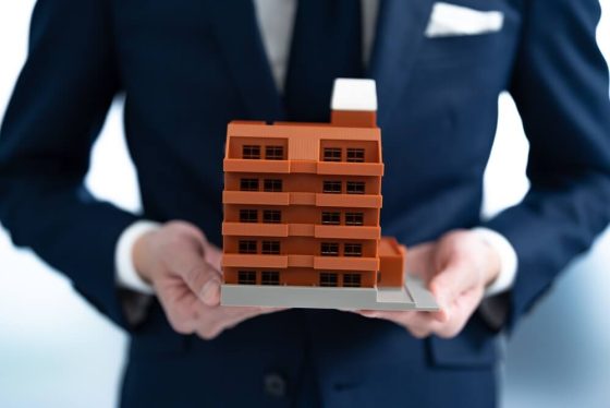 Man's hands holding miniature apartment building, importance of renters insurance in California.