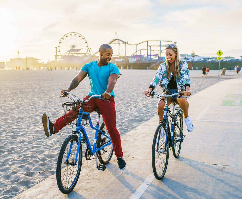 Couple having fun riding bikes together at Santa Monica California. How to sign up for car insurance and health insurance when you move to California.