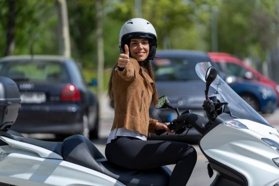 Female motorcyclist wearing a white helmet on a white bike giving a thumbs up, happy about insurance tips for motorcycle owners in California.