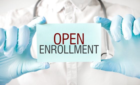 Healthcare professional holds an Open Enrollment sign explaining what Open Enrollment is for insurance coverage.