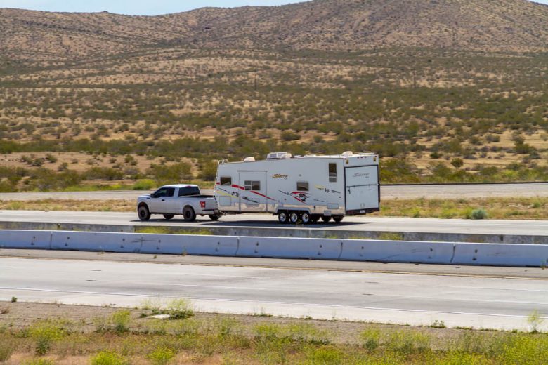 Pickup truck towing a travel trailer on a desert highway towing trailer insurance California.